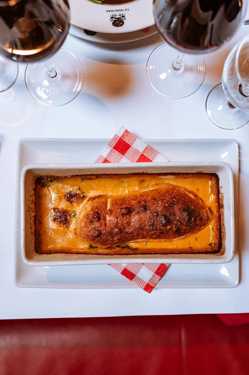 A close-up of a baked, rectangular pie on a table with white linen and red wine glasses.