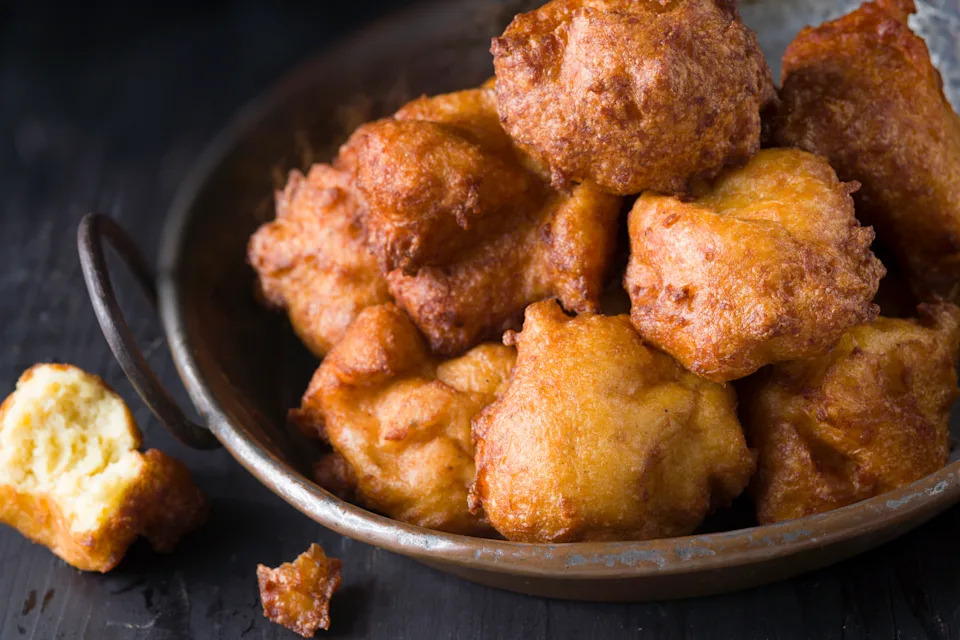 A close up of french fried potato puffs or pommes dauphine in a metal dish on a black table.