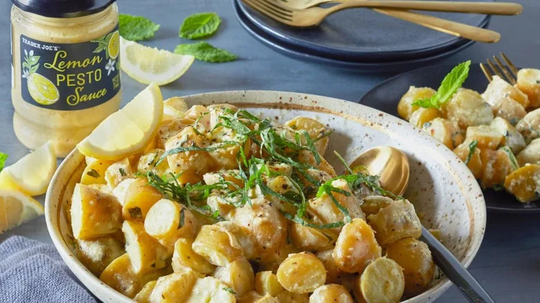 Trader Joe's lemon pesto sauce mixed with potatoes that are served in a bowl and topped with herbs and a lemon wedge