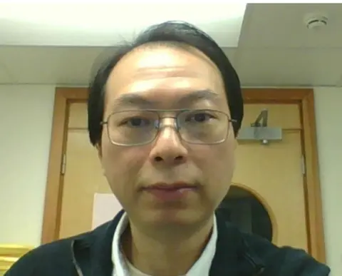 University of Leicester Dr Thong Cao wearing glasses with short hair in front of a wooden door.