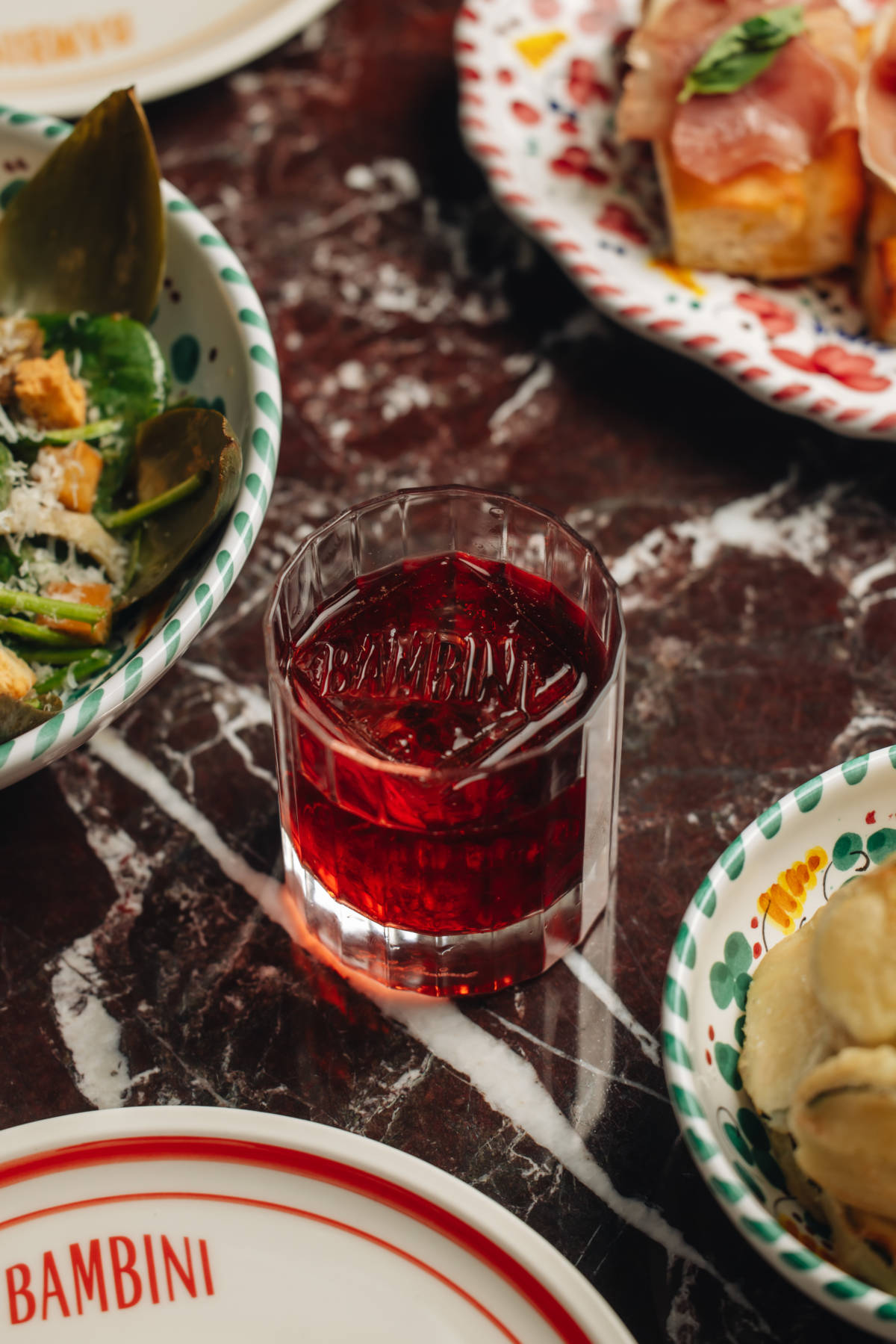 a negroni in the middle of the table with glimpses visible of italian dishes