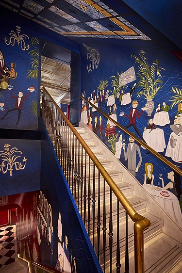 staircase with ornate railing and vibrant wall murals depicting people, a dining scene, and lush foliage