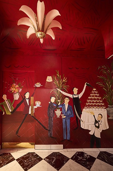 Artistic mural of elegantly dressed waitstaff serving drinks and desserts on a vibrant red wall beneath an ornate light fixture.