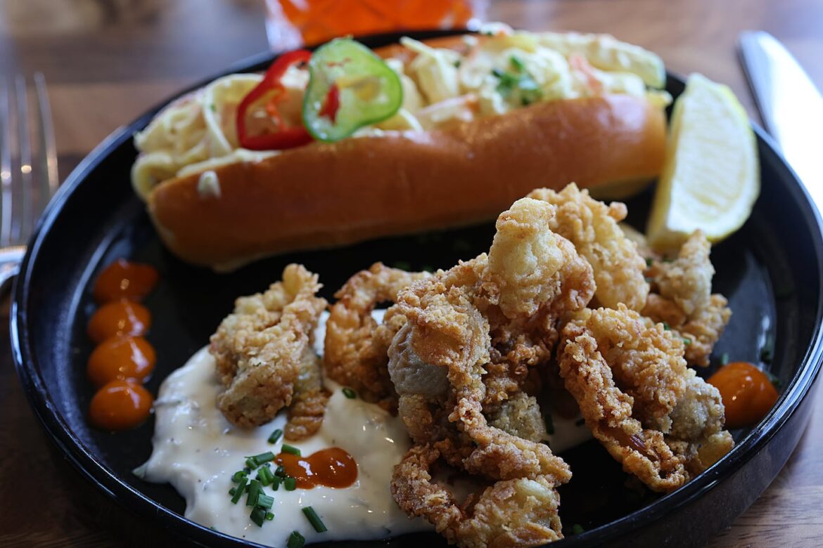 Luna Mare in Ipswich is serving Greek and Mediterranean specialties Fried clams with aioli beside a top-loading brioche roll holding apple slaw.