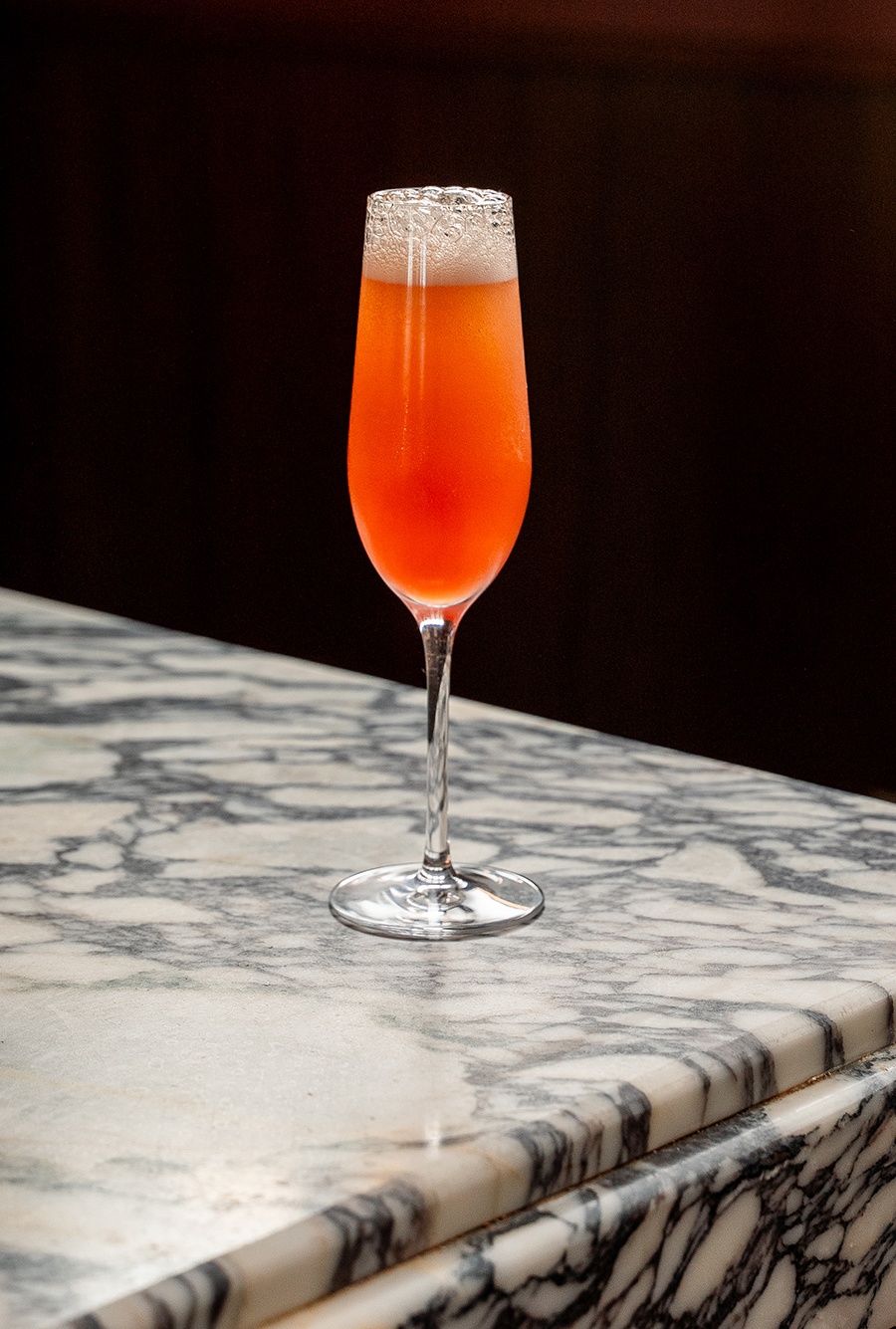 A pink sparkling cocktail on a marble bar.