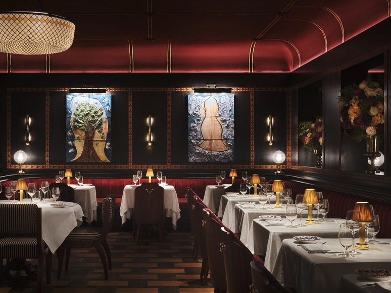 Elegant restaurant interior with dim lighting, tables set with white cloths, red booths, and artistic wall decor.