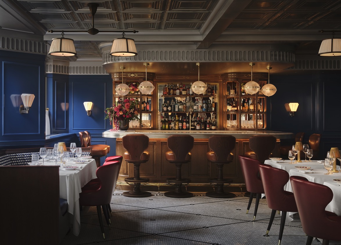 Elegant restaurant interior with a warmly lit bar, cushioned chairs, and set tables, creating a cozy dining atmosphere.