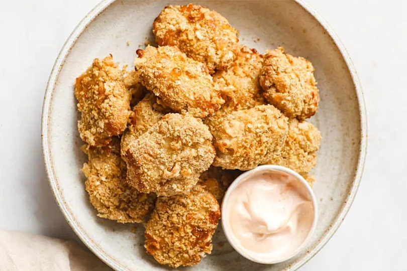 Chicken nuggets on a plate with a cup of dipping sauce.