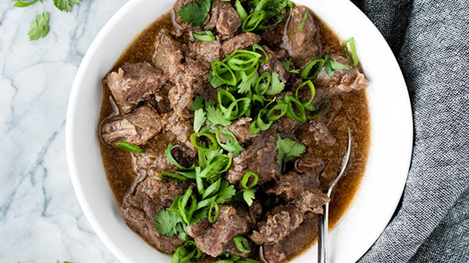 Bowl of Korean barbecue beef with sliced green onions and cilantro, featuring tender beef chunks in dark savory sauce with a spoon.