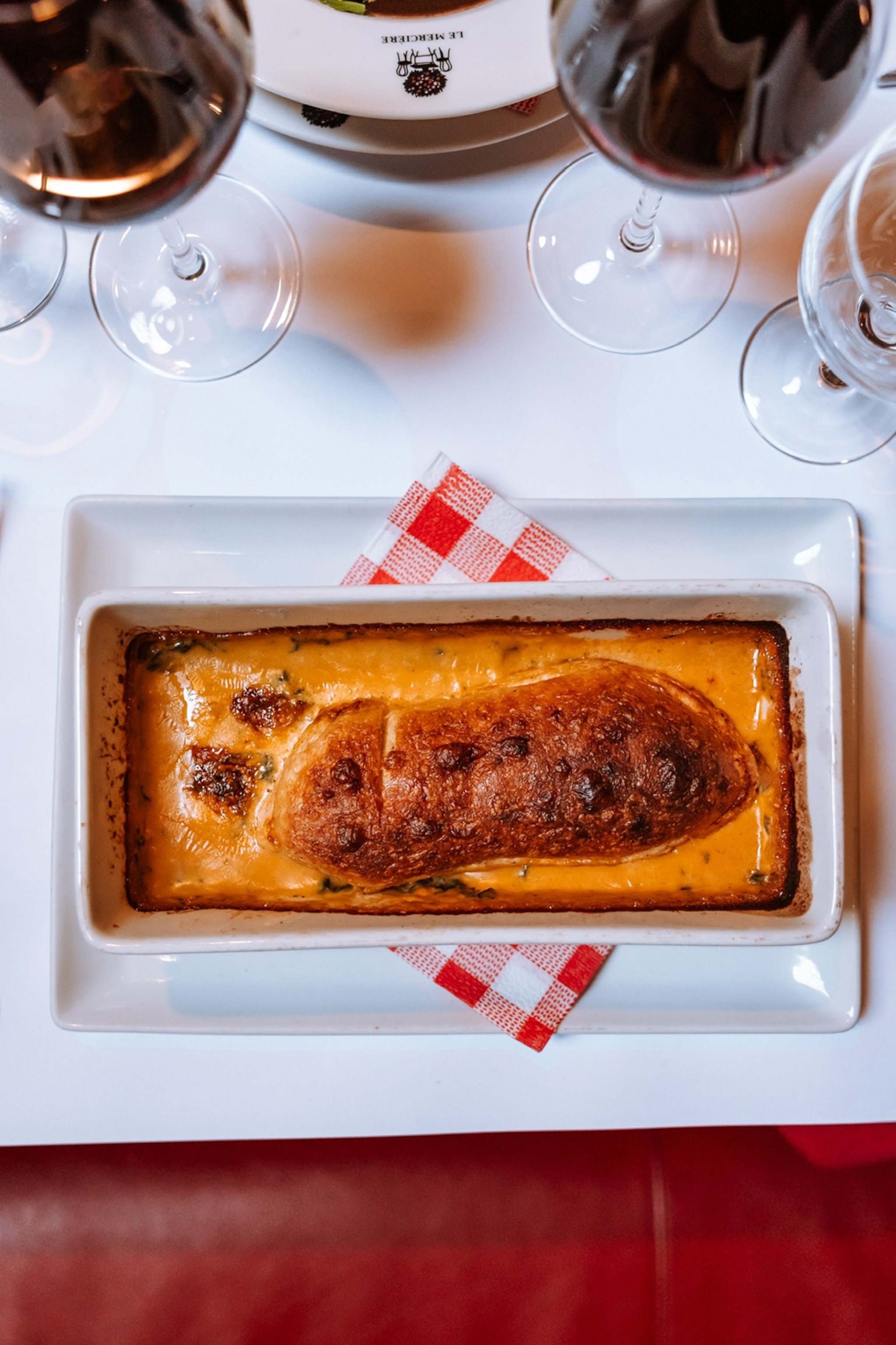 A close-up of a baked, rectangular pie on a table with white linen and red wine glasses.