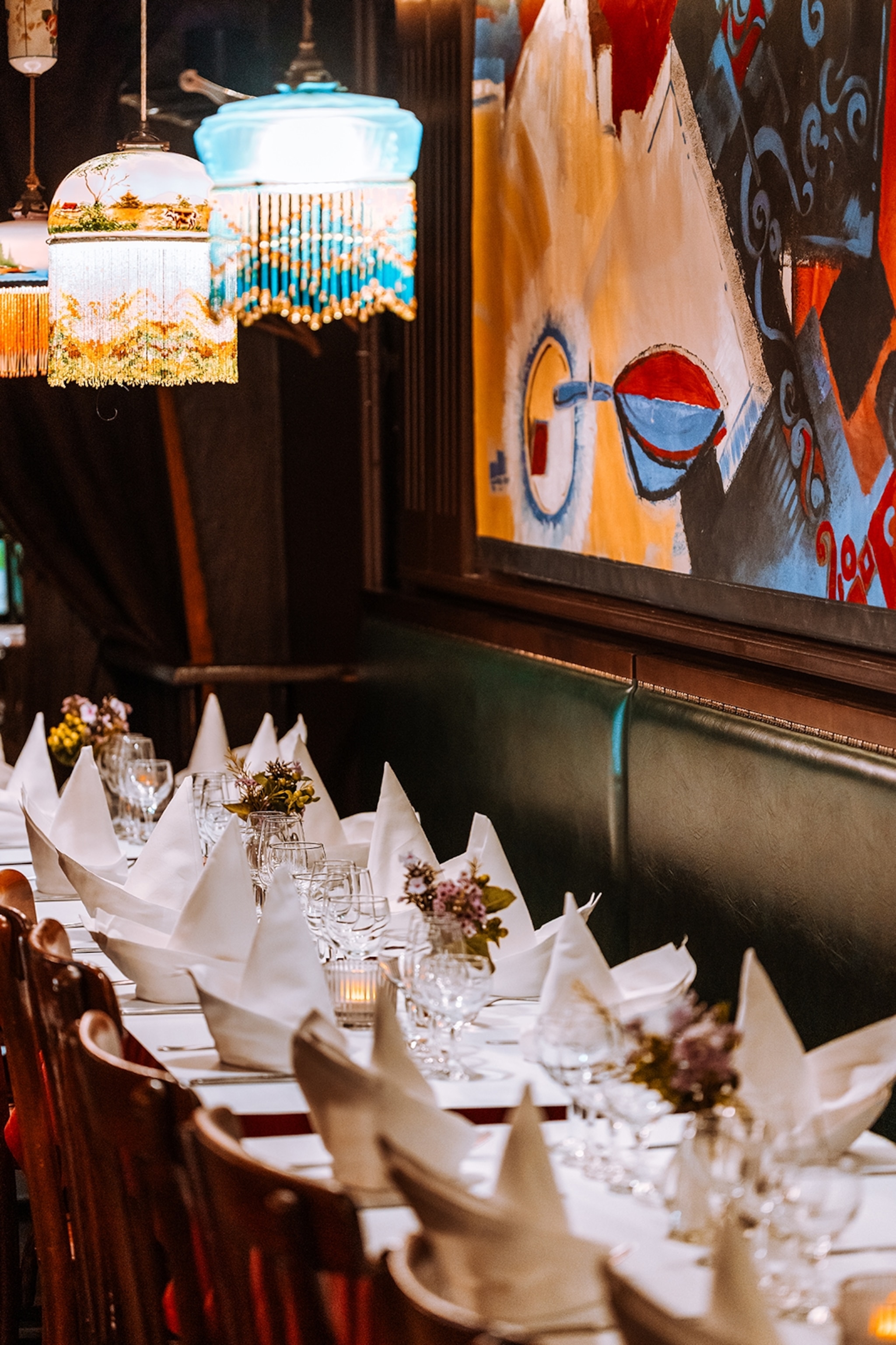 A long restaurant table with modern art hung on the wall, leather sofa benches, bistro chairs and beaded lamps hung from the ceiling.