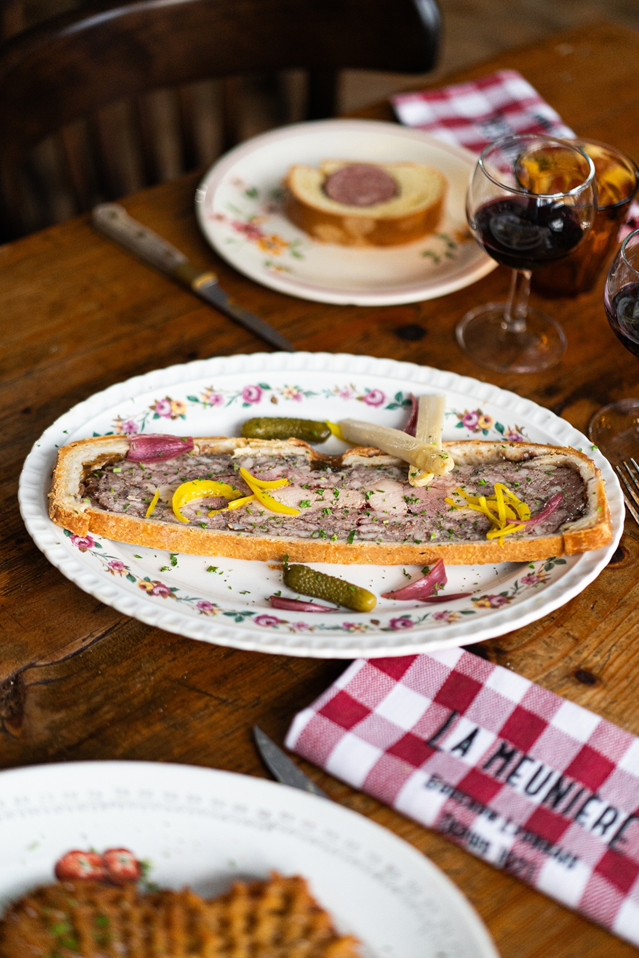 A close-up shot of a terrine topped with pickles on a rustic table with a linen napkin.