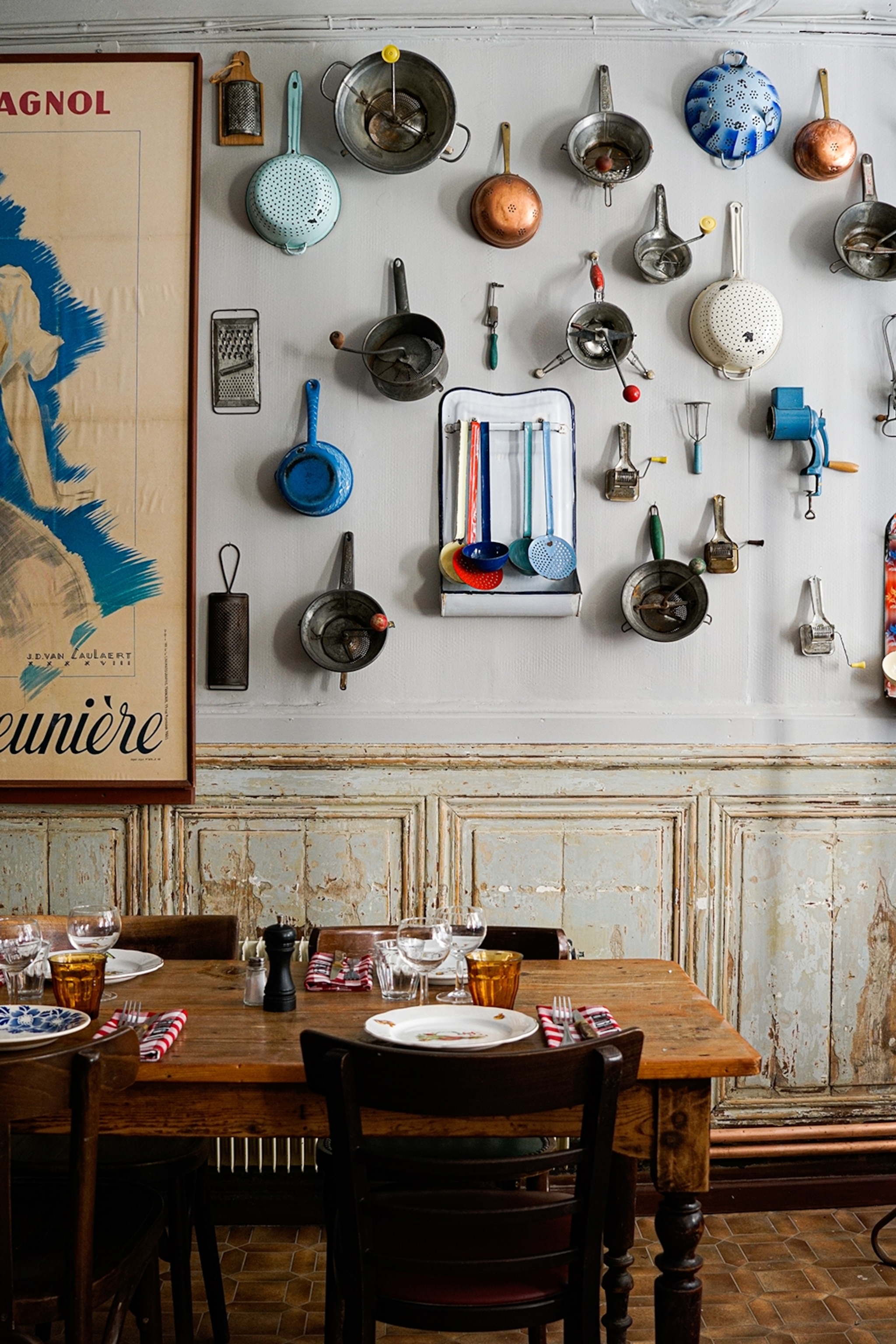 The interiors of a rustic yet modern restaurant with a French painting hung next to countless pans and pots on the wall.