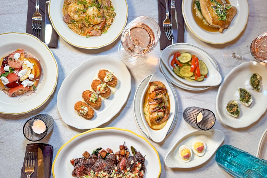 Overhead shot of a plate of food, including croquettes, baked oysters, hanger steak, shrimp and grits, and more.
