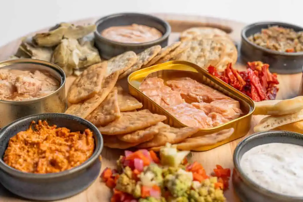 aerial view of a plate of food. There are a selection of meat slices, cheeses, nuts and fruit, along with multiple dipping sauces all aranged on a nice wood board 