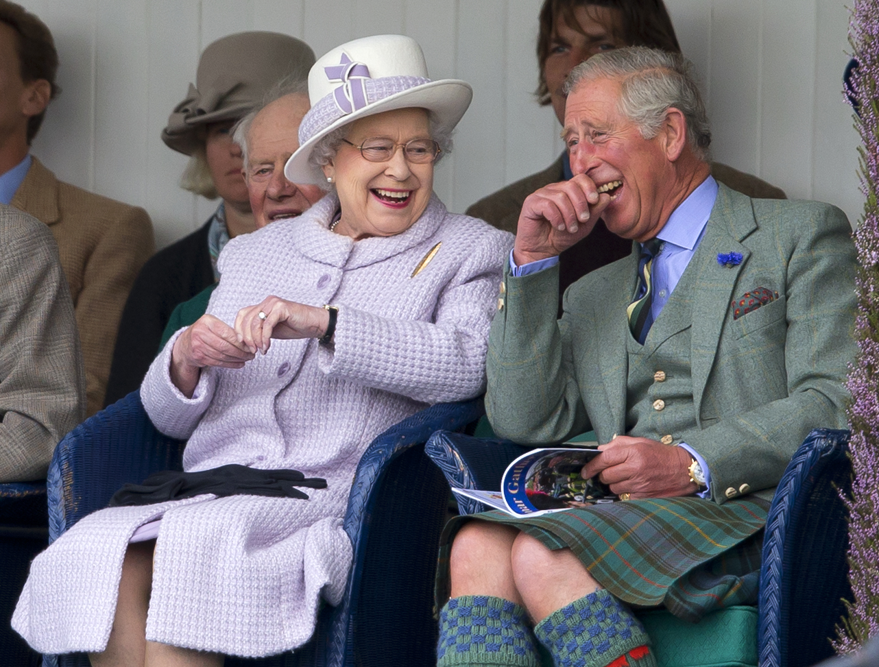 Queen Elizabeth wearing a lavender coat and sitting next to Prince Charles laughing