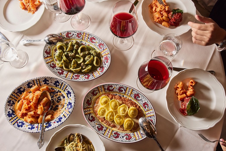 A variety of Italian pasta dishes and glasses of red wine on a white tablecloth.