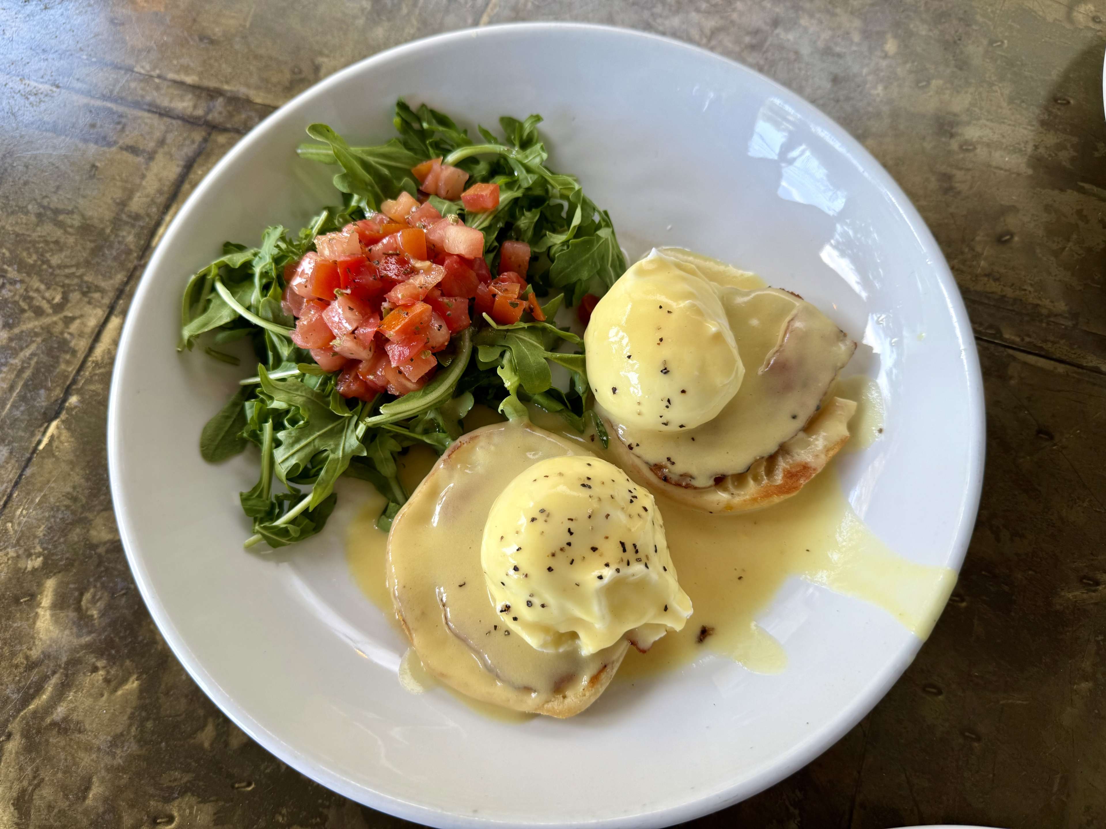 A plate of eggs benedict with a side salad of arugula.