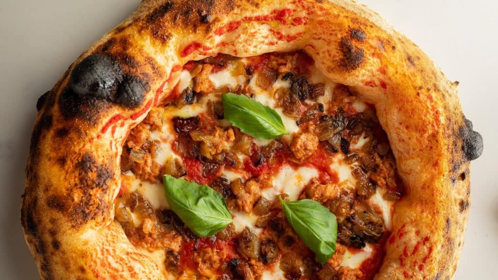 an oven-baked pizza with a puffy crust topped with basil leaves