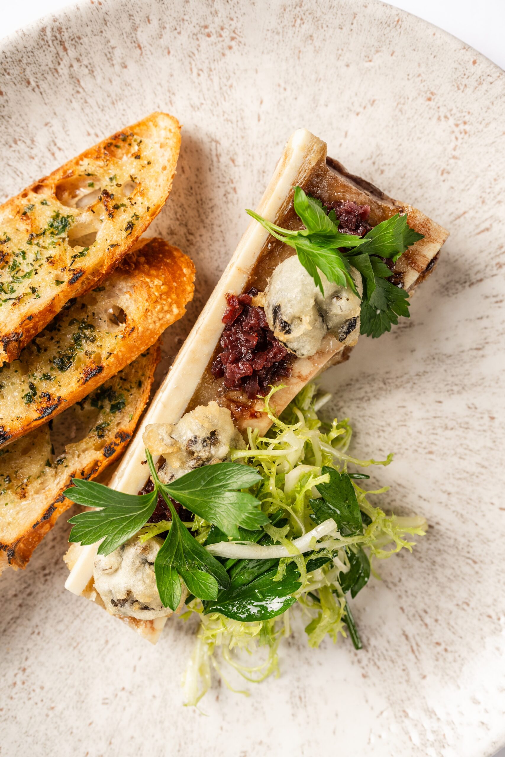 The roasted bone marrow iat Annabelle Brasserie is topped with shallot bacon jam, tempura-fried escargot, and spears of grilled bread ($28). Photo Brian Kennedy.
