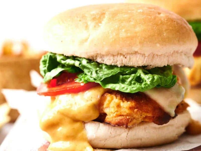 A close-up of a chicken sandwich with melted cheese, lettuce, and tomato in a soft bun.