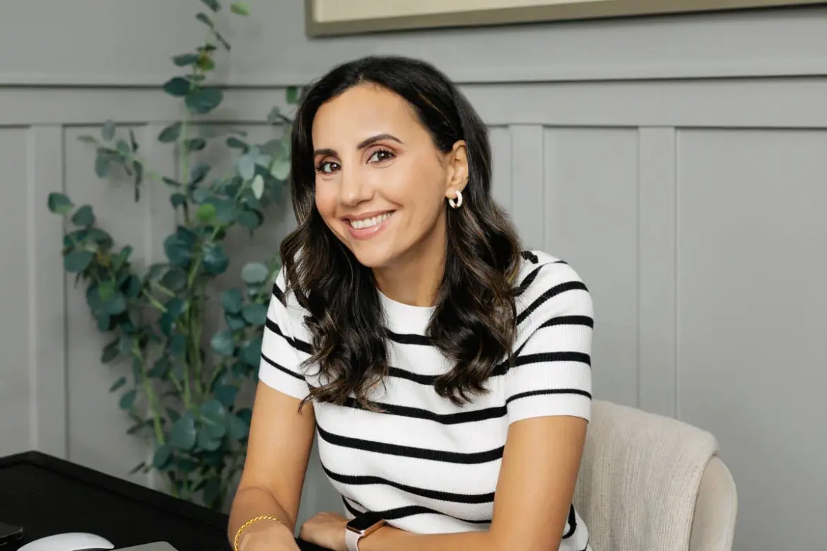 Yumna Jawad, founder of Feel Good Foodie, smiling while seated at her desk in a bright home kitchen setting.