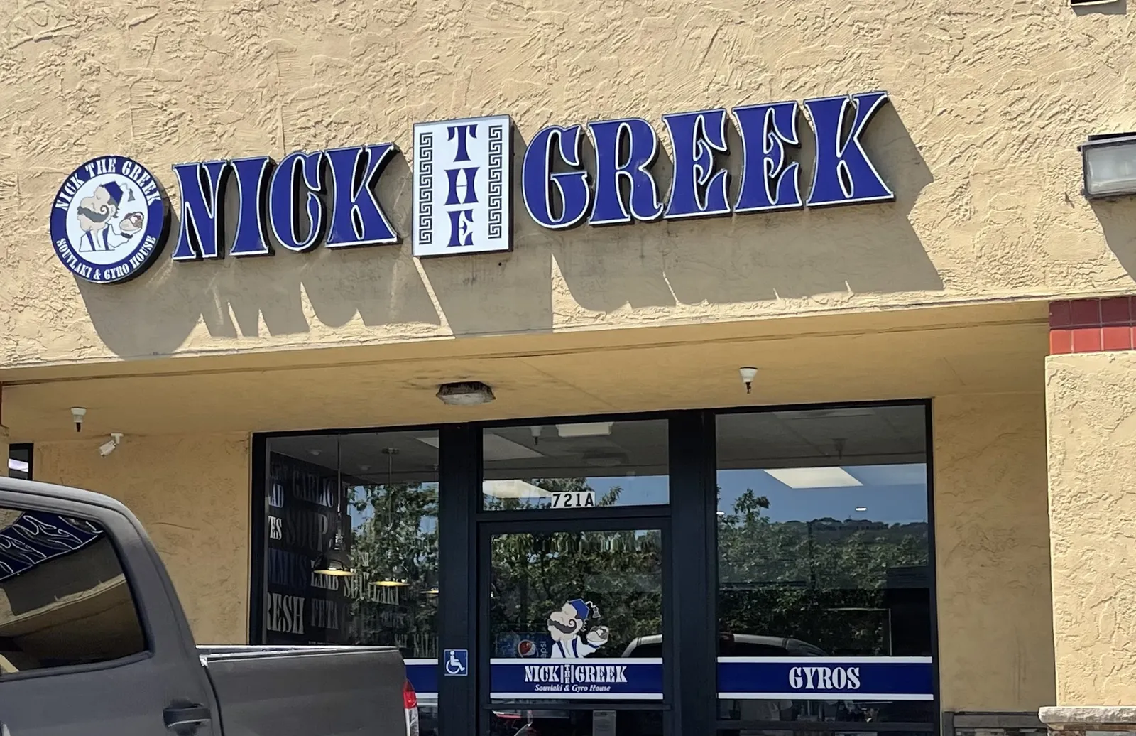 An image of a beige building with a blue sign that says Nick the Greek