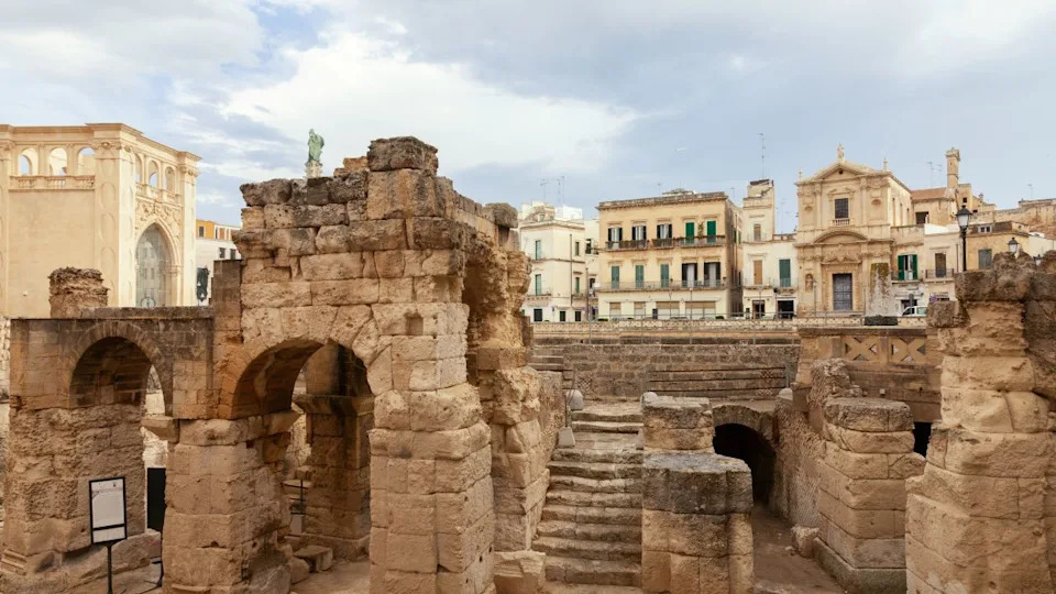 An aerial shot of grunge exterior buildings with old stone arch gates with blue sly in Lecce, Italy