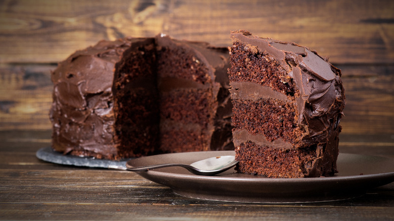 Round devil's food cake with a slice cut out of it and sitting next to the cake on another plate