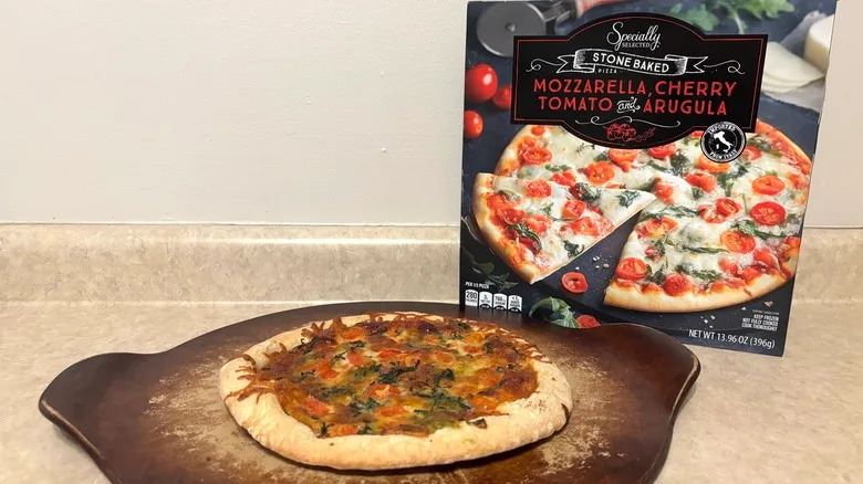 Mozzarella, cherry tomato, and arugula pizza on baking stone and box on a neutral background.