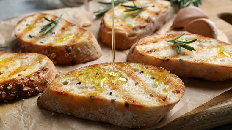 Olive oil being drizzled onto toasted bread with fresh rosemary
