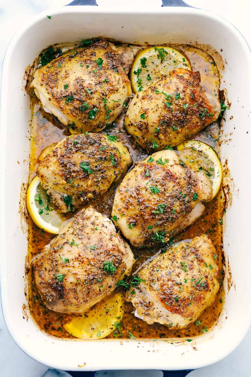 Baked Chicken Thighs are tender, juicy chicken thighs baked in an AMAZING glaze mixture of Italian seasoning, Dijon mustard, sweet honey a pinch of spice and garlic cloves. This is a MUST make family meal! Baked chicken thighs in a baking pan with lemon slices.
