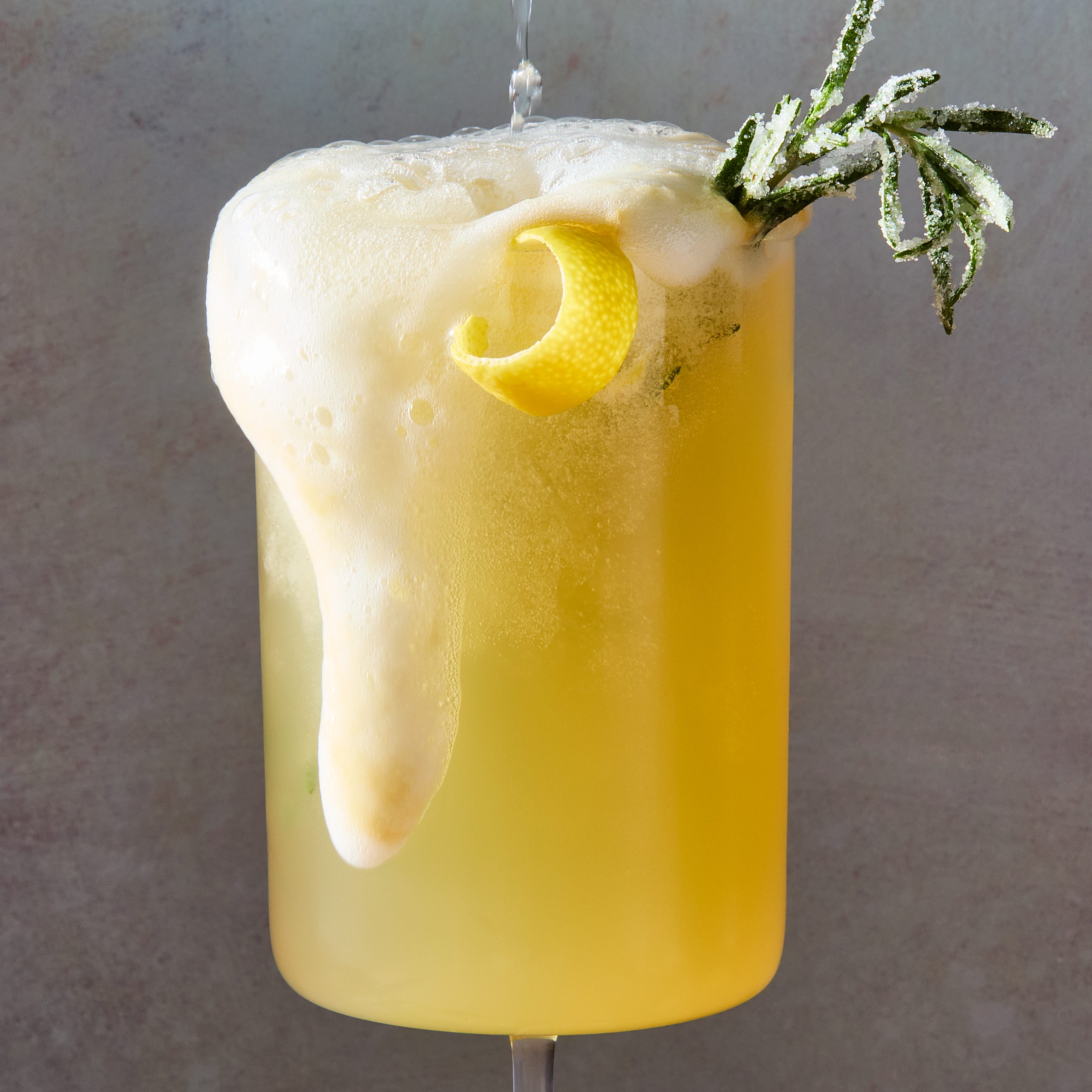 bee's knees mocktail spritz with a lemon twist and sugared rosemary