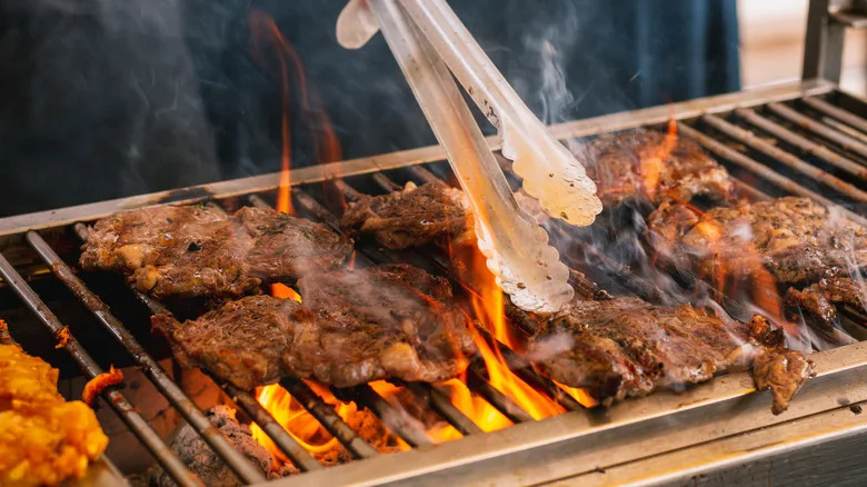 metal tongs hovering over steaks on a bbq grate