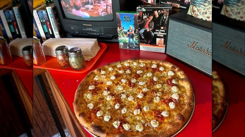 A whole pizza on a counter at Chrissy's Pizza in front of a small TV and VHS tapes