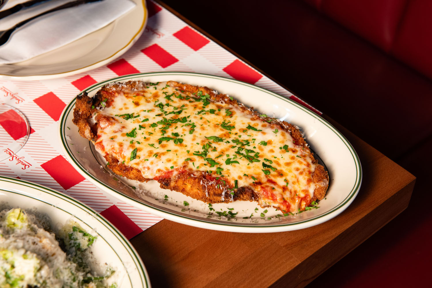 Chicken parm sitting on a table with a Caesar salad at Sunday Sauce.