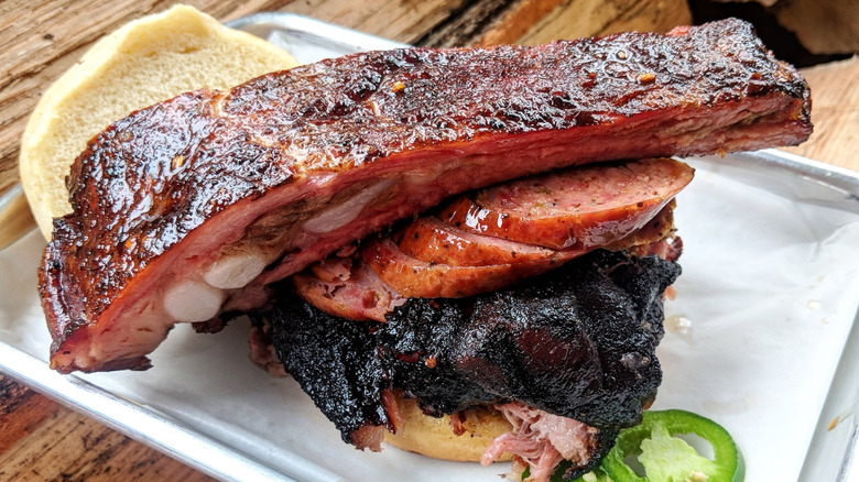 Barbecue brisket, sausauge, and a beef rib stacked on a bun