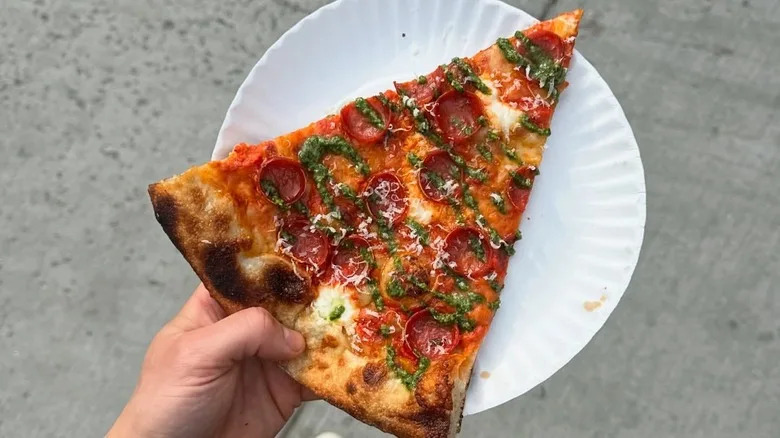 A slice of pizza from Jonny's Pizza in NYC, on a paper plate held by a person out of frame