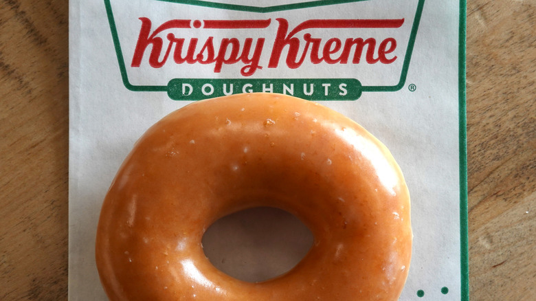 One plain glazed Krispy Kreme doughnut on a napkin with the Krispy Kreme logo at the top