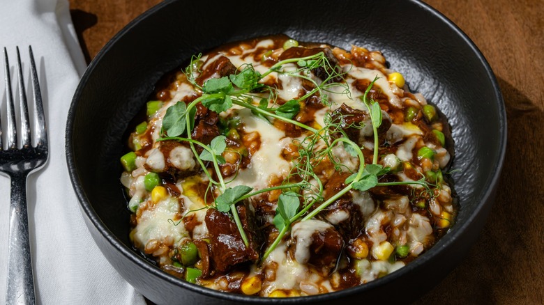 Black bowl of stewed meat with cheese, and microgreens