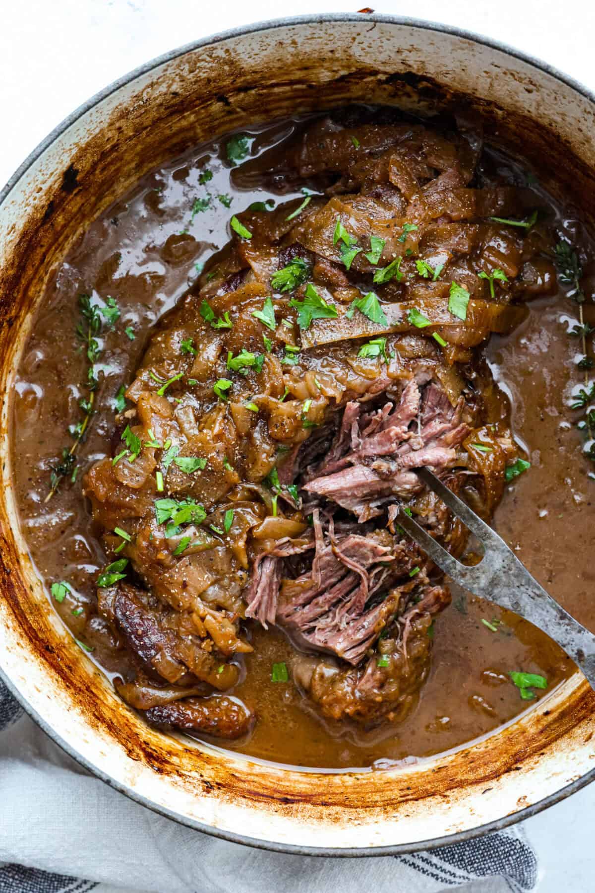 This French Onion Pot Roast is pure comfort food! Slow-cooked to perfection, the roast becomes melt-in-your-mouth tender as it simmers in a rich, savory gravy infused with the deep, caramelized flavor of onions. Overhead shot of cooked French onion pot roast in the dutch oven.