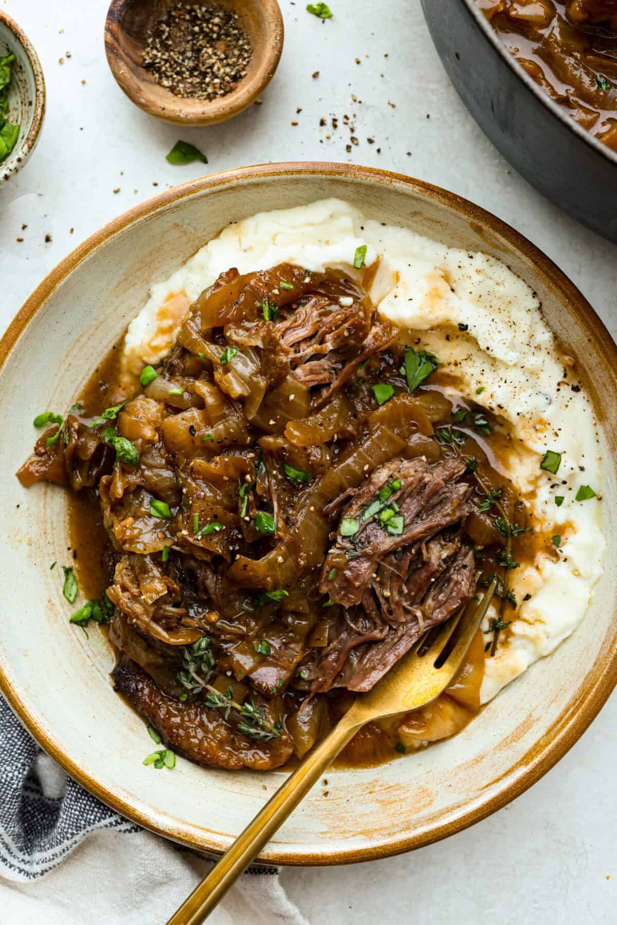 This French Onion Pot Roast is pure comfort food! Slow-cooked to perfection, the roast becomes melt-in-your-mouth tender as it simmers in a rich, savory gravy infused with the deep, caramelized flavor of onions. Plate of mashed potatoes and french onion pot roast with a golden spoon.