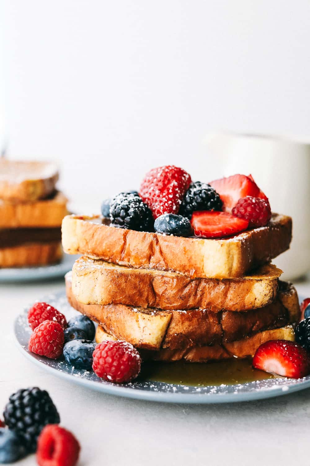 French Toast is a sliced thick, chunky bread dipped in a creamy egg, milk and cinnamon mixture with a secret ingredient that will take this French toast over the top! A little slice of heaven on your plate! French toast stacked up with berries and powdered sugar on them.