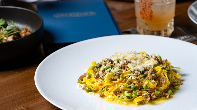 Pasta dish with fresh peas, meat, and garnished with freshly grated parmesan cheese on a white plate