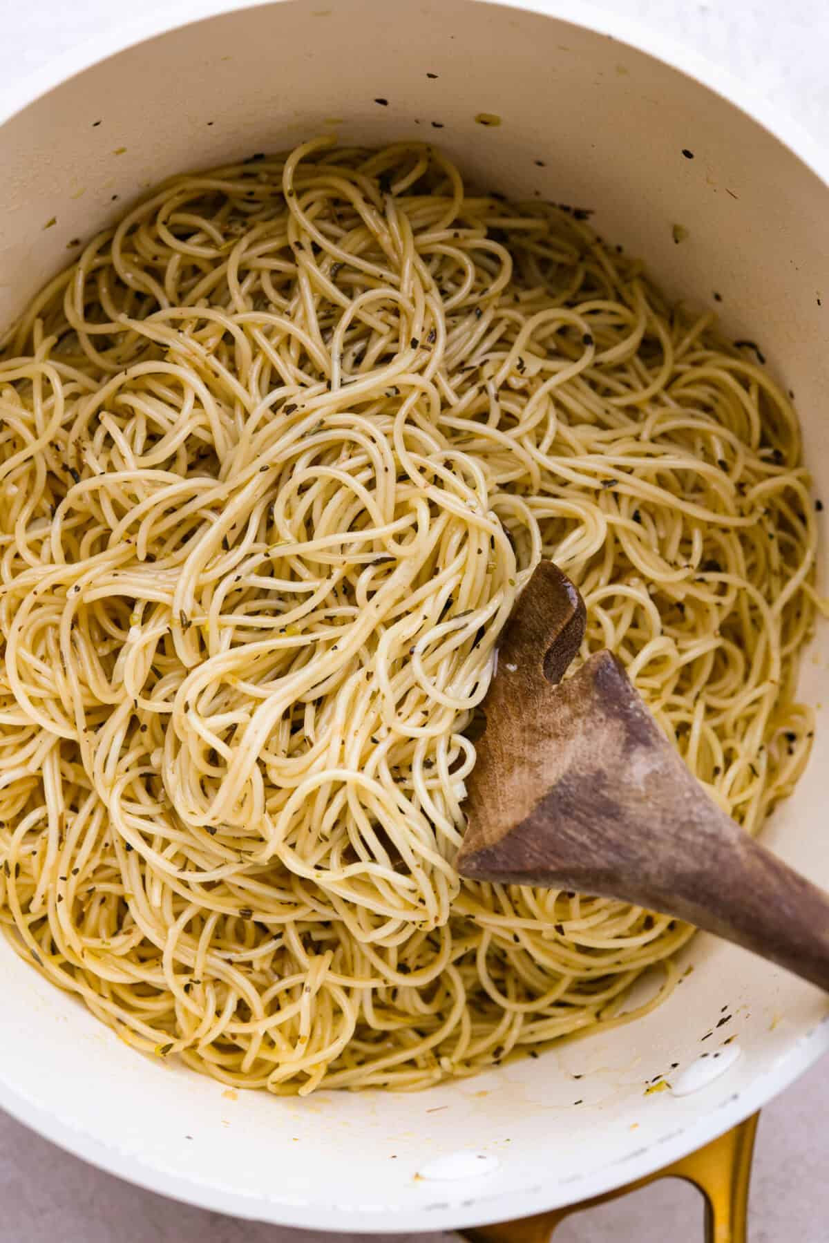 Garlic butter pasta is a quick and simple dish yet packed with flavor. Angel hair pasta is bathed in a buttery garlic sauce and topped with Italian seasoning. Overhead shot of garlic butter pasta in a pot with wooden slotted spoon.