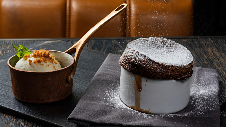 Chocolate souffle in a white ramekin next to a scoop of ice cream in a small pan