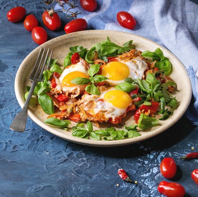 Traditional Israeli Cuisine dishes Shakshuka Fried egg with vegetables tomatoes and paprika in ceramic plate with cloth, herbs and ingredients above over blue texture background Copy space