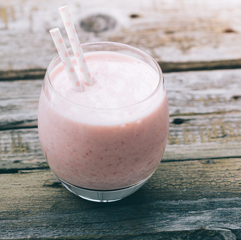 Strawberry pink smoothie in a glass with a straw on a old wooden rustic table. Toned image. Summer and healthy lifestyle concept.