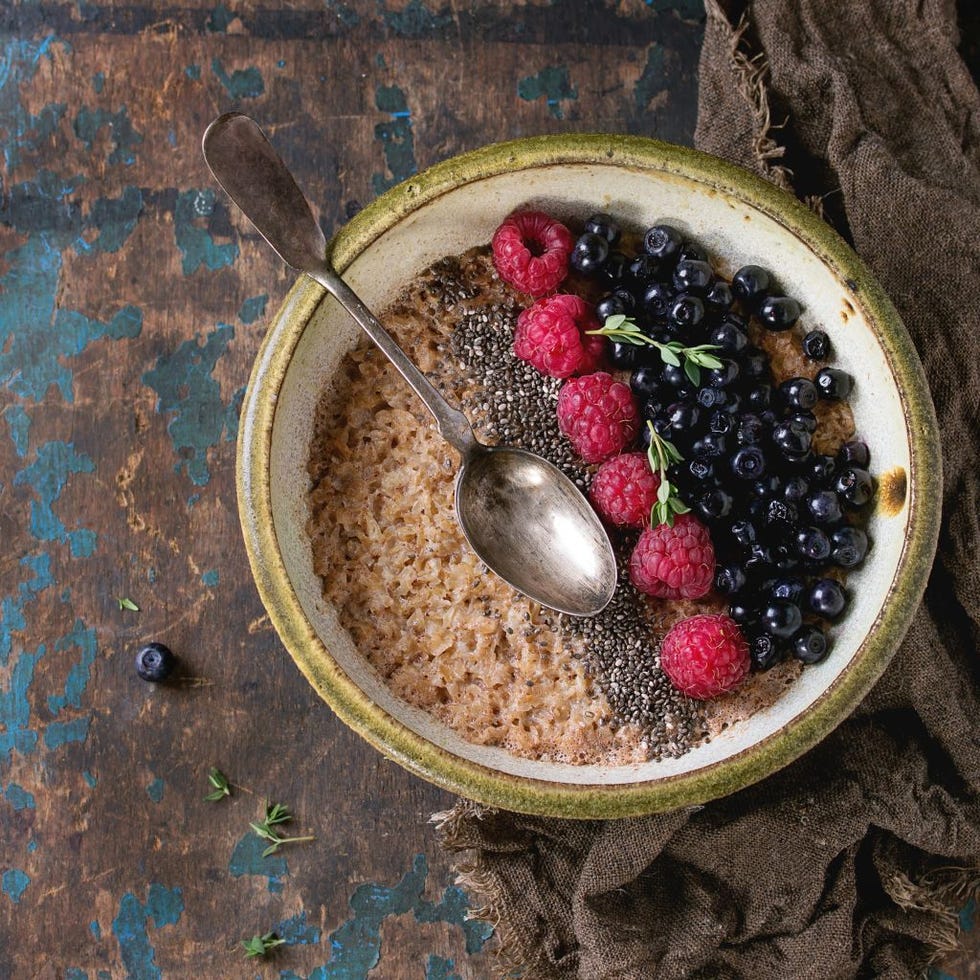 Bowl of oatmeal porridge with blueberries, raspberries and chia seeds, served with sackcloth rag and vintage spoon over old wood textured background. Rustic breakfast theme. Top view, space for text