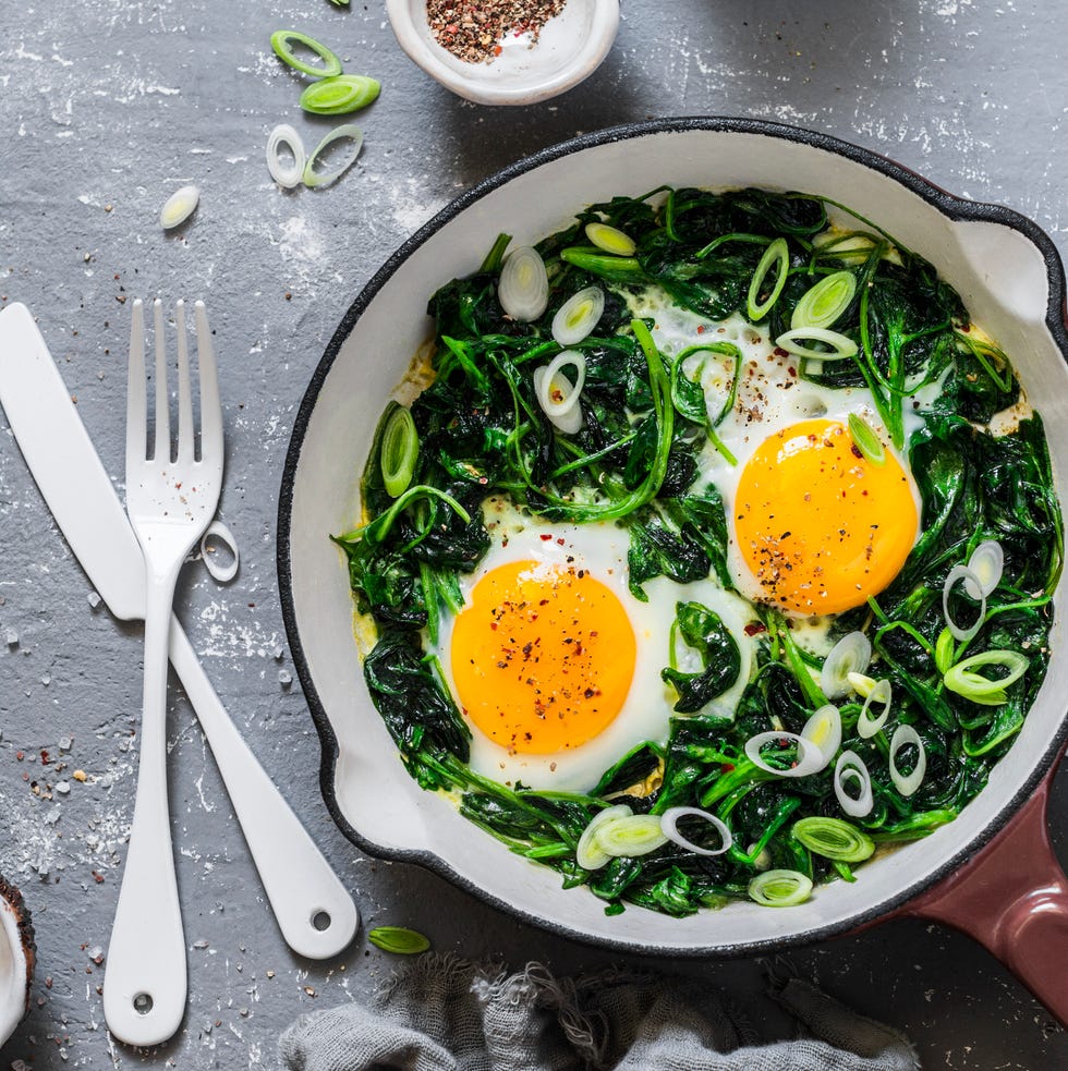 Green shakshuka. Fried eggs with fresh spinach, ramson, leek in a pan on a gray background, top view